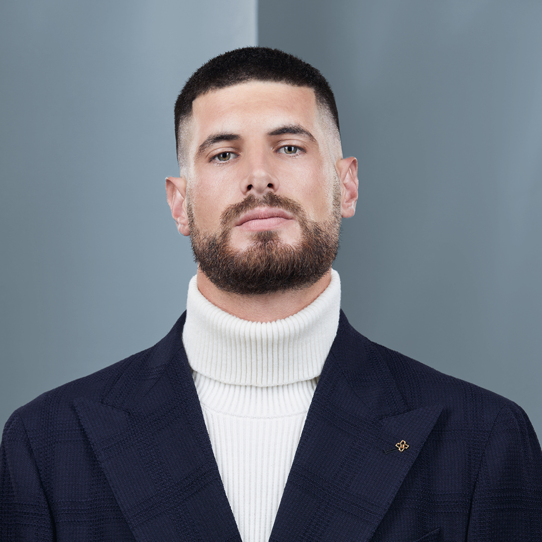 ragazzo, con capelli quasi rasato, giacca blue sotto maglietta bianca. Sguardo molto serio